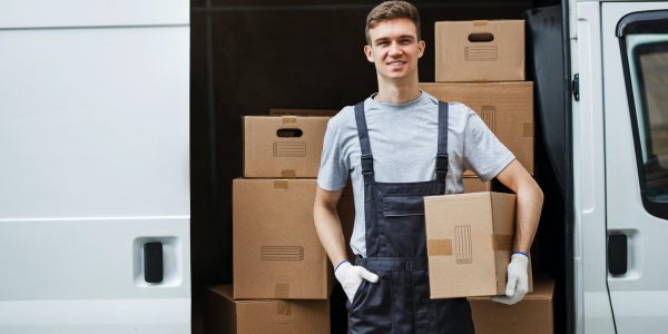 a-young-handsome-smiling-worker-wearing-uniform-is-standing-next-to-the-van-full-of-boxes-holding-a.jpg